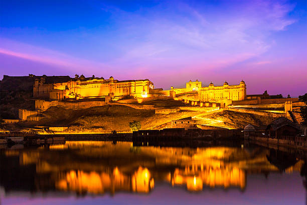 Indian landmark - Amer Fort (Amber Fort) illuminated at night - one of principal attractions in Jaipur, Rajastan, India refelcting in Maota lake in twilight