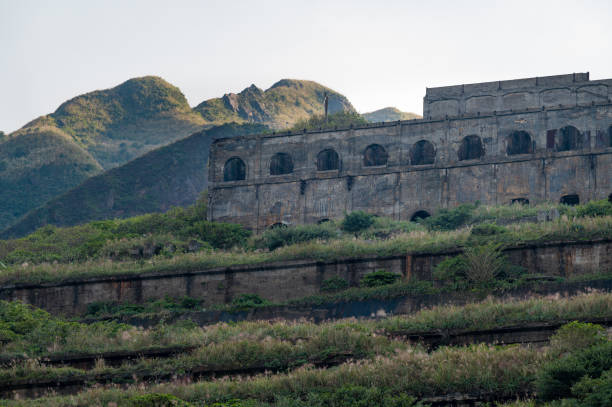 Abandoned mine factory standing on the hill full of grass, in the distance sunlight shines on the peak, in New Taipei City, Taiwan.